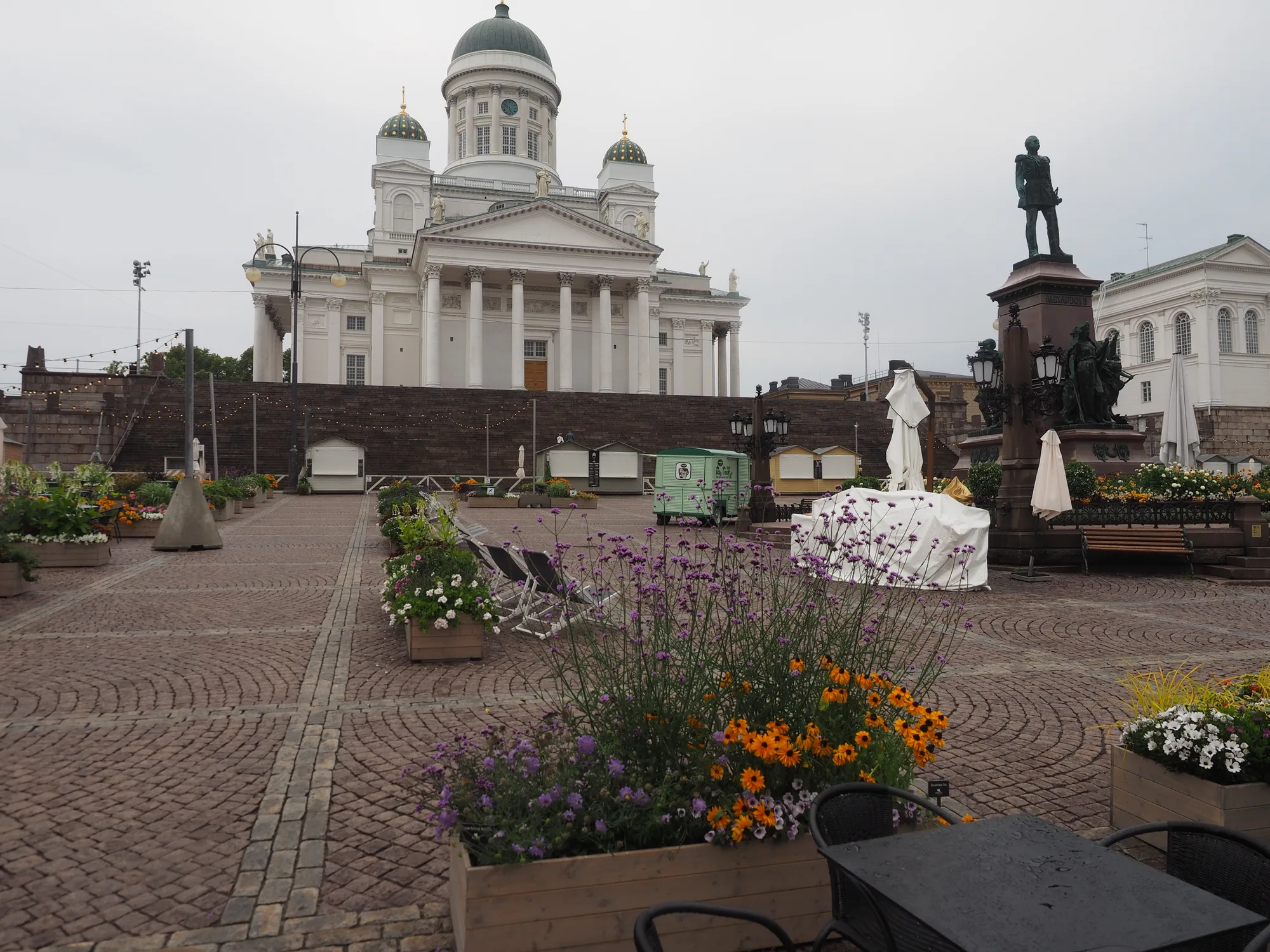 Helsinki Cathedral with its white facade and green domes above Senate Square, with the Alexander II statue and flower planters in front