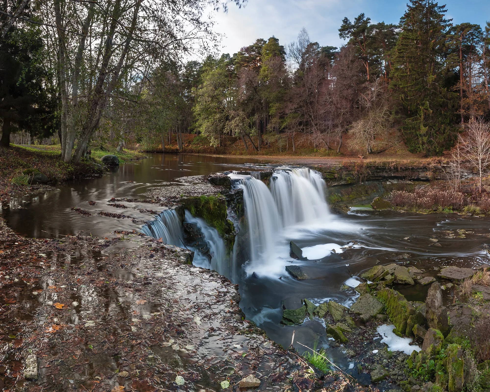 The wide Keila-Joa waterfall cascading over a rock ledge in a wooded park, Estonia