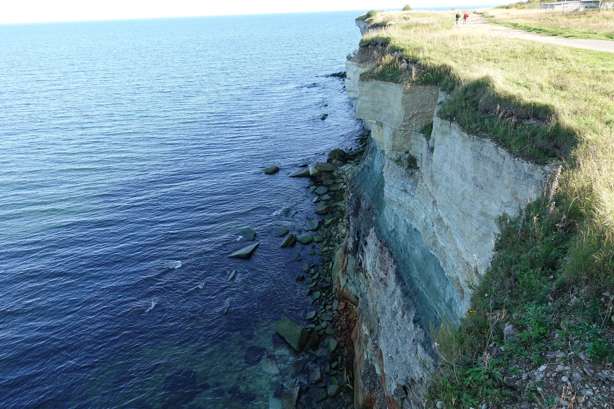The layered limestone Pakri sea cliffs dropping to the blue Baltic Sea near Paldiski, Estonia, with walkers on the clifftop for scale