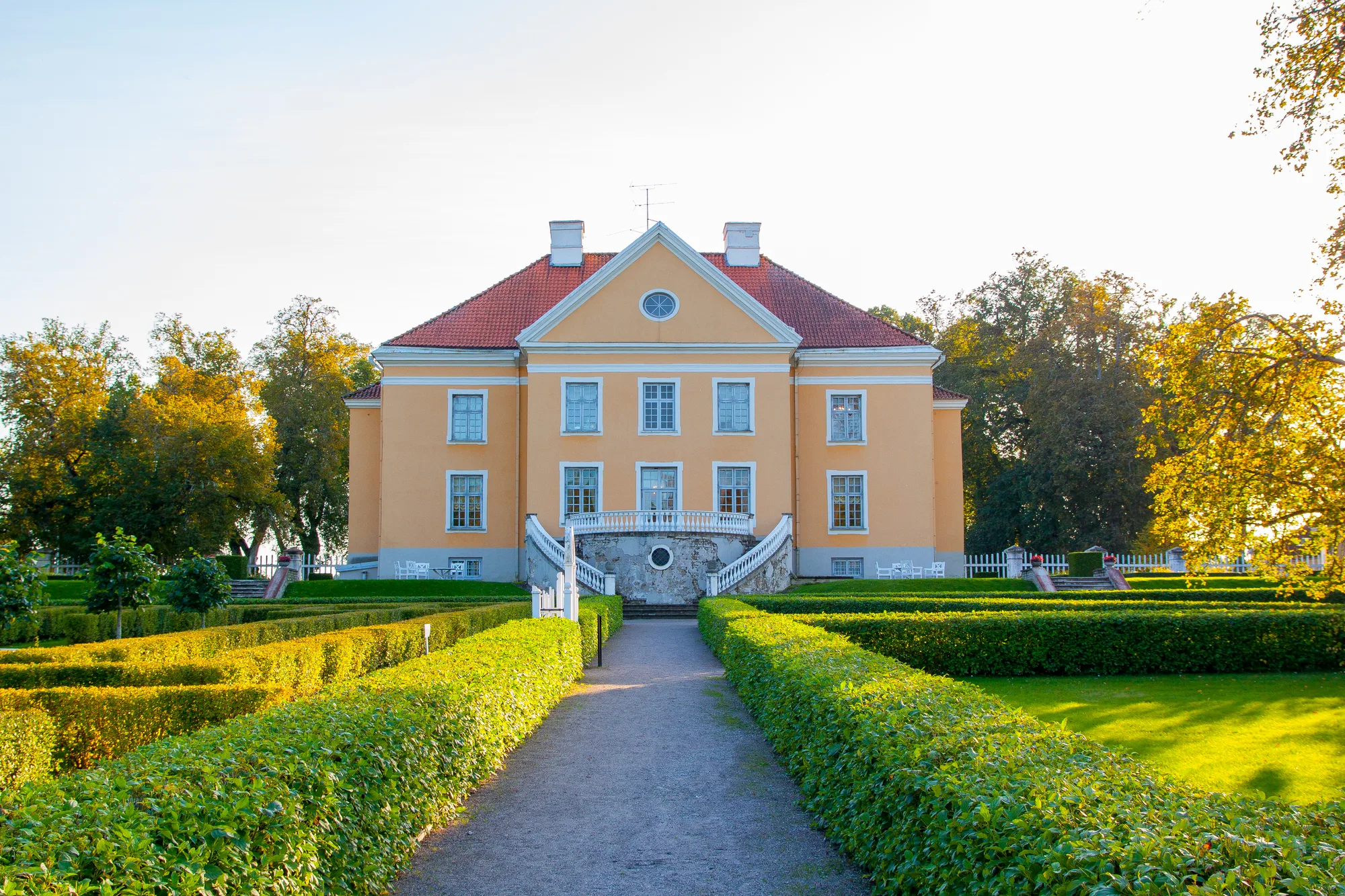 The yellow Baroque Palmse Manor house with red tiled roof and curved staircase, across its formal hedge garden, Lahemaa, Estonia