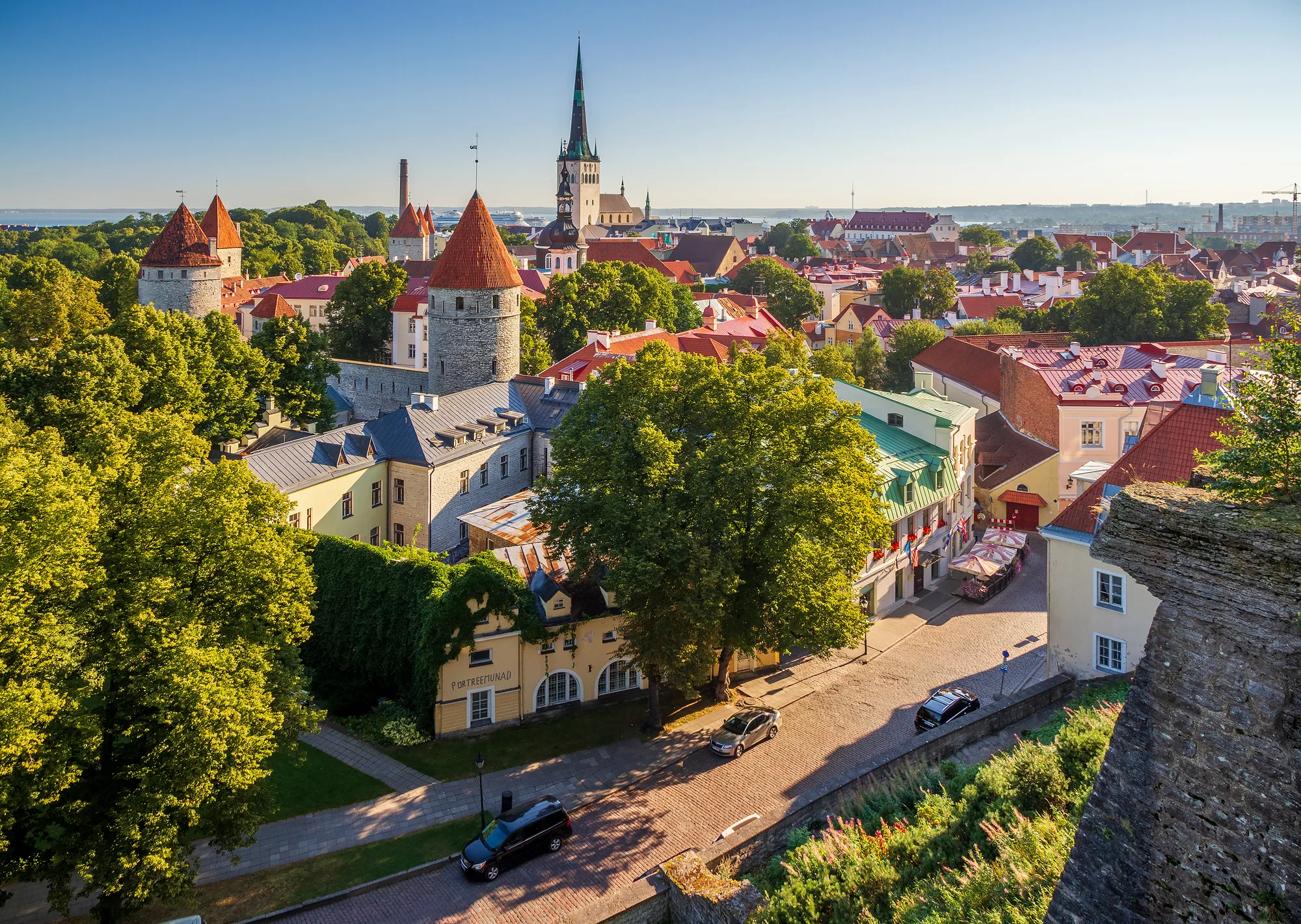 View of Tallinn Old Town from the Patkuli viewing platform: red-roofed city-wall towers, rooftops, St Olaf's spire and the sea in evening light
