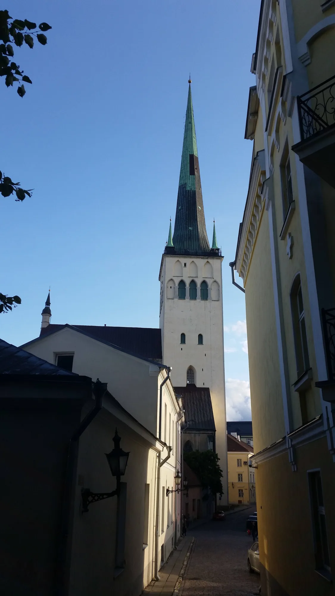 St Olaf's Church (Oleviste kirik) in Tallinn, its white tower topped by a very tall green copper needle-spire, seen down a cobbled lane